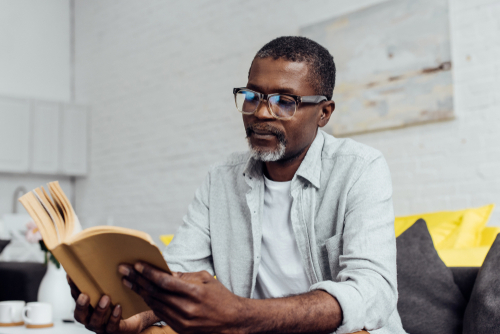 man wearing glasses while sitting on the couch and reading a book