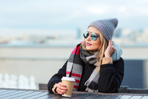 woman in winter clothing and sunglasses sitting at table with cup of coffee